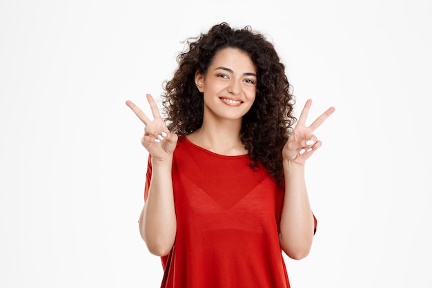 Tender curly girl smiling and showing peace gesture