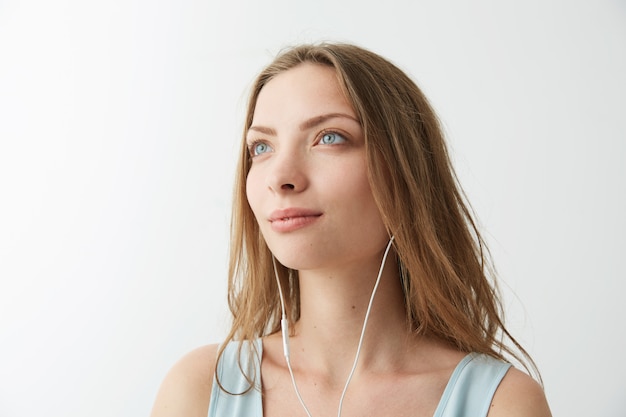 Tender dreamy young pretty girl dreaming listening to streaming music in headphones .