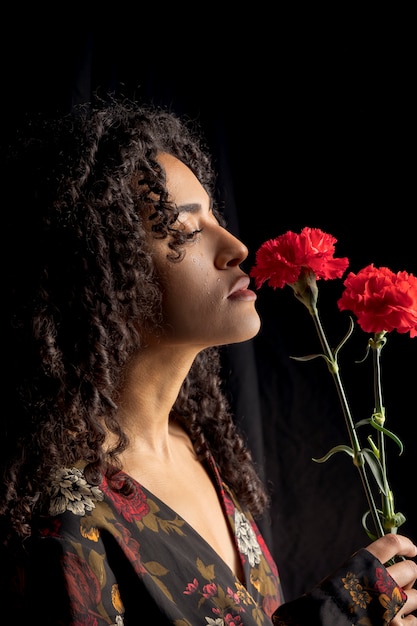 Tender ethnic woman with flowers in darkness