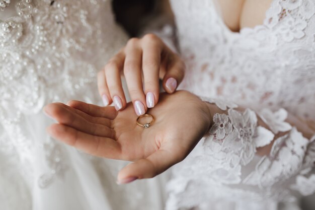 Tender golden engagement ring with diamond on woman's hand with manicure and wedding dress decollete