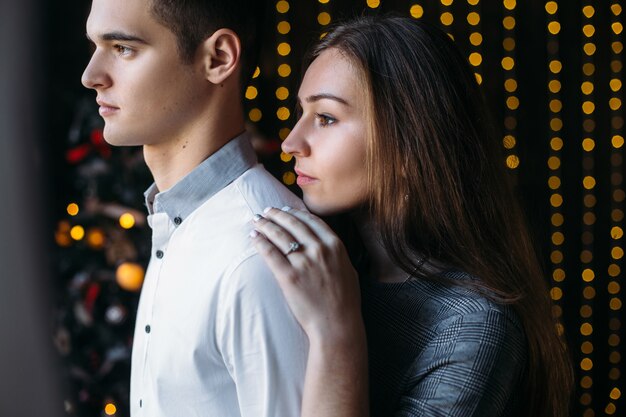 Tender hugs of beautiful couple standing in the room with cosy winter holidays decor