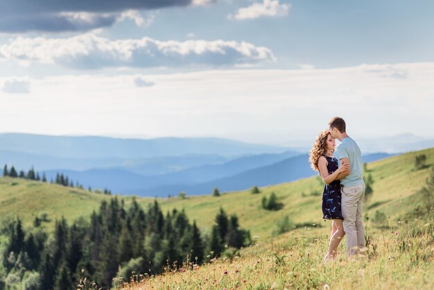 Tender hugs of a couple standing on a green hill before gorgeous landscape