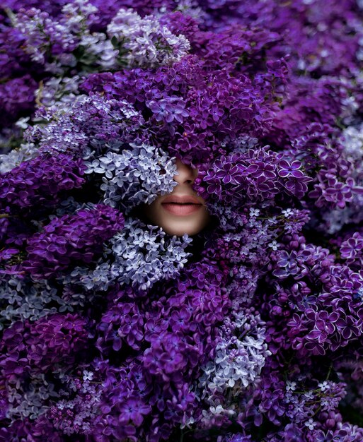 Tender lips of young caucasian girl surrounded with lots of violet lilac, wallpaper, spring melody