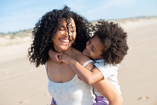 Tender mother and daughter spending time on beach. African American family walking, laughing, playing, riding on back. Leisure, family time, parenthood concept