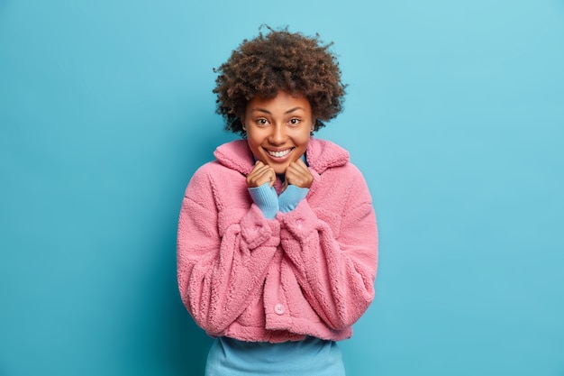 Tender pleased dark skinned young woman smiles lovely keeps hands under chin