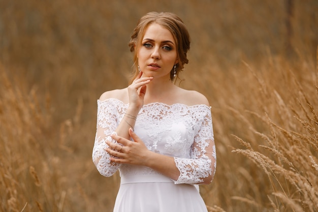 Tender portrait of bride in white dress with veil outdoors in sunny day. wedding day on the nature. cute womans face close up. beautiful bride with hairstyle and make up in  wheat field