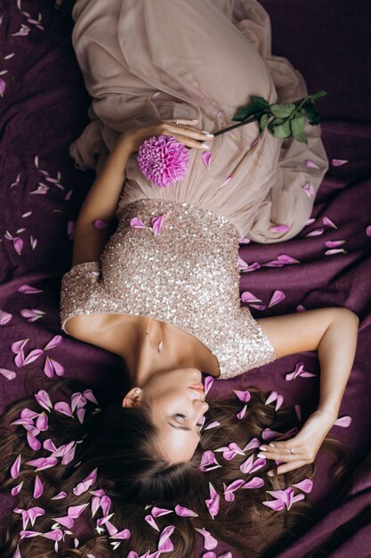 tender pregnant woman in pink dress lying on violet plaid covered with pink petals