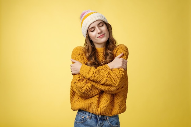 Tender sensual charming young girlfriend dreaming close eyes flirty smiling tilting head embracing herself recalling nice romantic memories wanna hold boyfriend tight, cuddling yellow background