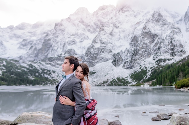결혼식 복장에 부드러운 미소 커플은 아름다운 겨울 산 풍경 앞에 서있다