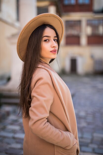 Нежная улыбающаяся леди идет по улице и позирует в повседневной современной куртке и шляпе