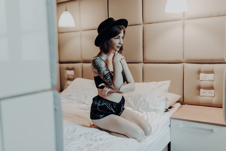 無料Photo 朝のベッドに座っているファッション黒下着と広い帽子の優しい小さな女性