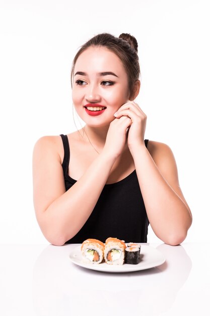 Tender young woman is sitting at the white table and have a plate with sushi