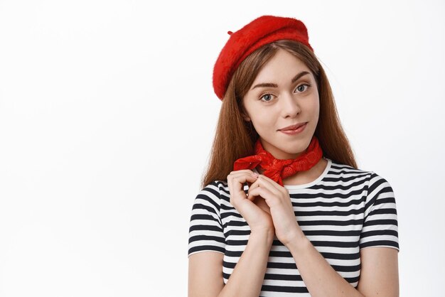 Tender young woman looking with cute and lovely face at camera wearing berret and striped tshirt standing over white background