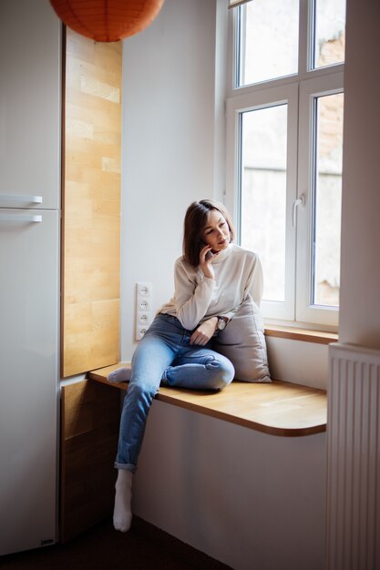 ブルージーンズと白いtシャツの広いwindowhillに座っている優しい若い女性