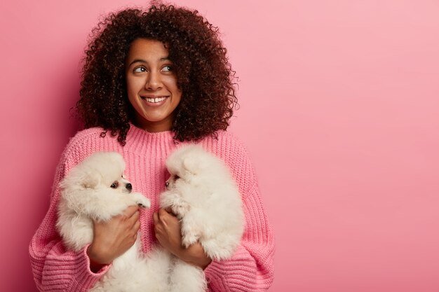 Tenderness, animal care and people concept. Girl pet owner poses with two fluffy cute puppies, have friendly relationship