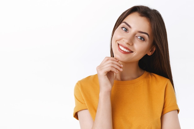 Tenderness, beauty and women concept. Sassy coquettish caucasian girl in yellow t-shirt, tilt head and smiling joyfully, touching chin gently, express sensuality and upbeat emotion, white background