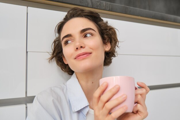 柔らかさとリラックス 若い女性はコーヒーを飲み 笑顔でリラックスし 紅茶を飲んで キッチンに座ります