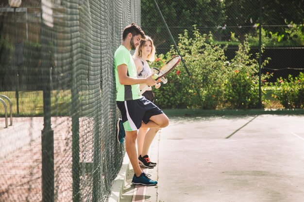 Tennis couple leaning at fence