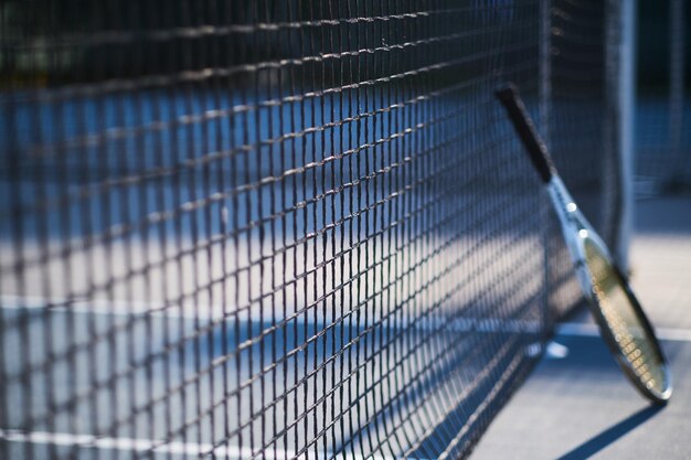 Теннисная ракетка стоит возле теннисной сетки снаружи в яркий солнечный день.