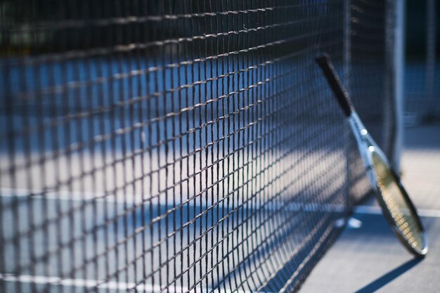 Tennis racquet is standing near tennis net outside at bright sunny day.