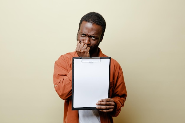 Tense grabbed chin young african american male holding clipboard isolated on white background