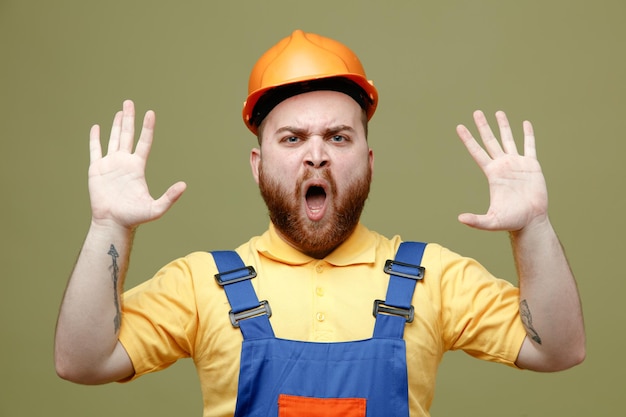 Tense spreading hands young builder man in uniform isolated on green background