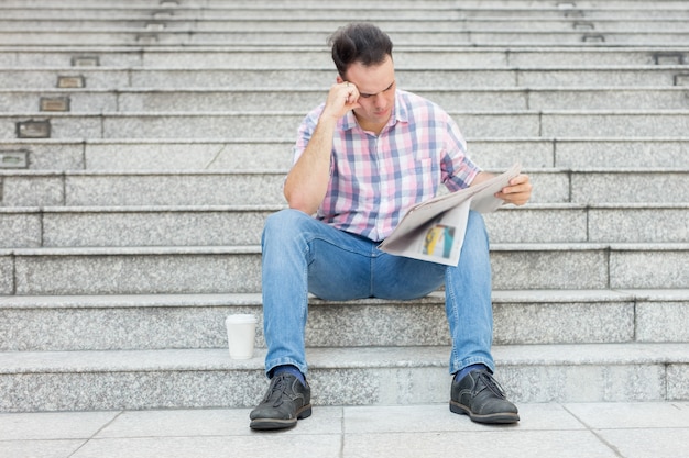 Free photo tensed man reading newspaper on city stairway