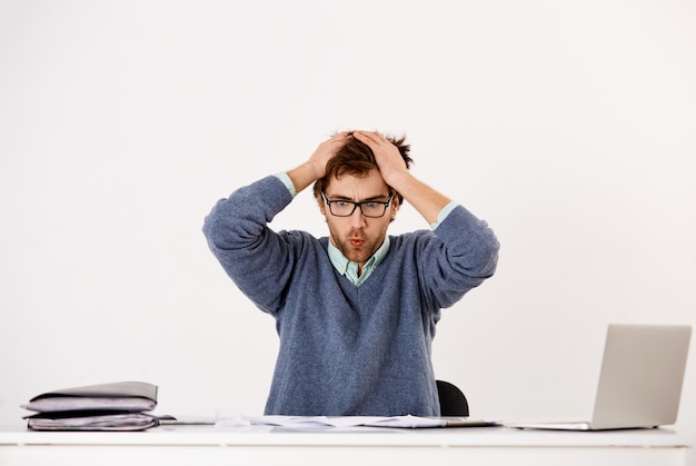 Free photo tensed and pressured young male employee, office worker or entrepreneur troubled, breathing-out as staring at documents and reports, cant deal with pressure of deadlines