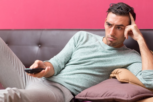 Free photo tensed young man changing tv channel at home