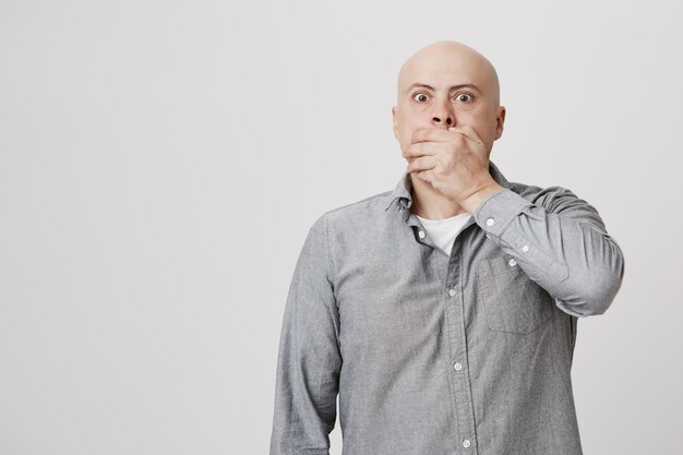 Terrified and shocked bald man cover mouth startled