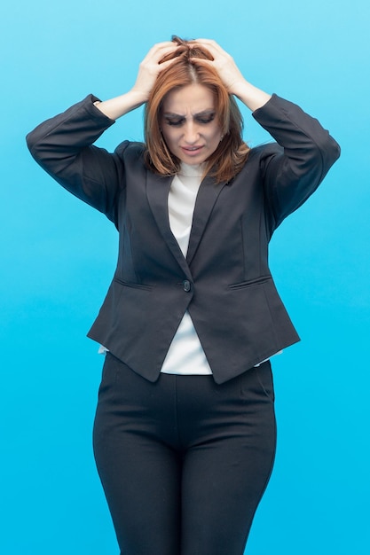 Terrified young lady put her hands to head and standing on blue background