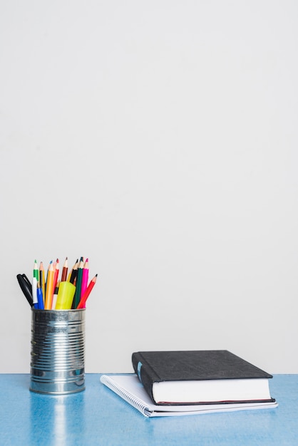 Textbook and notepad near tin cup with stationery