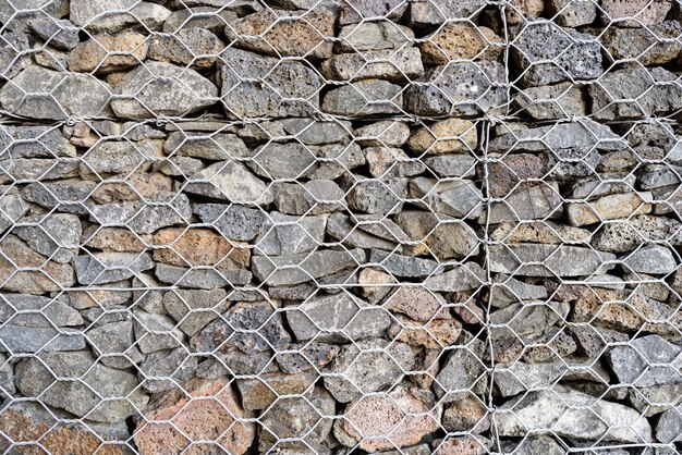 Textured background of Gabion, rock wall with wire meshed fence.