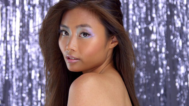 Thai asian model in studio with silver rain disco background and party makeup head and shoulders