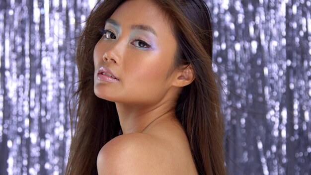 Thai asian model in studio with silver rain disco background and party makeup Ideal skin highlight makeup