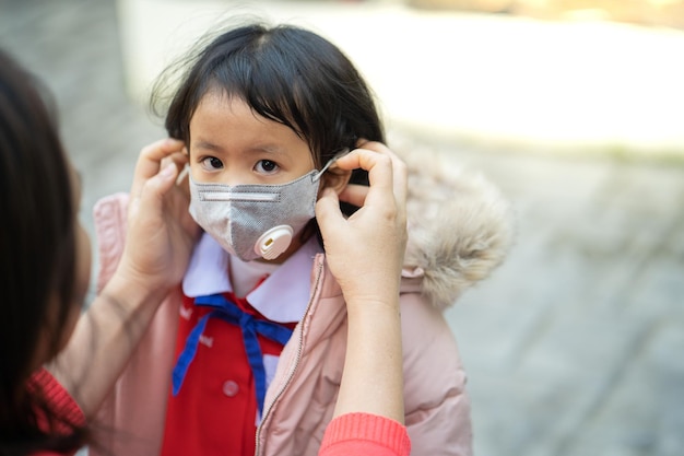 Madre tailandese che mette una maschera protettiva su sua figlia