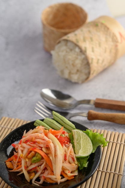 Thai papaya salad in a black plate with sticky rice