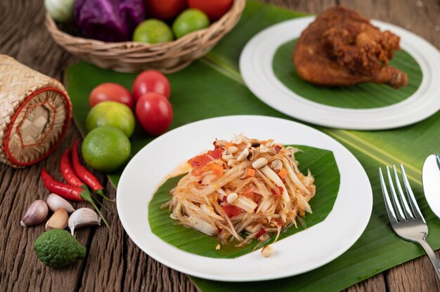 Insalata di papaya tailandese in un piatto bianco su foglie di banana con lime, pomodori, melanzane, peperoncino, aglio, peperoni, insalata e arachidi.