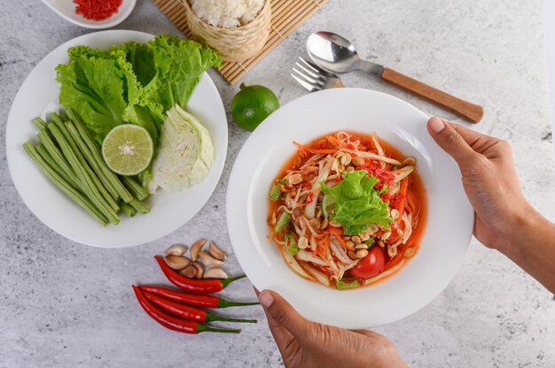 Thai papaya salad in a white plate with sticky rice and dried shrimps