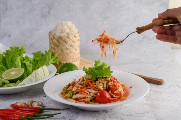 Insalata tailandese della papaia in un piatto bianco con riso appiccicoso e gamberetti essiccati