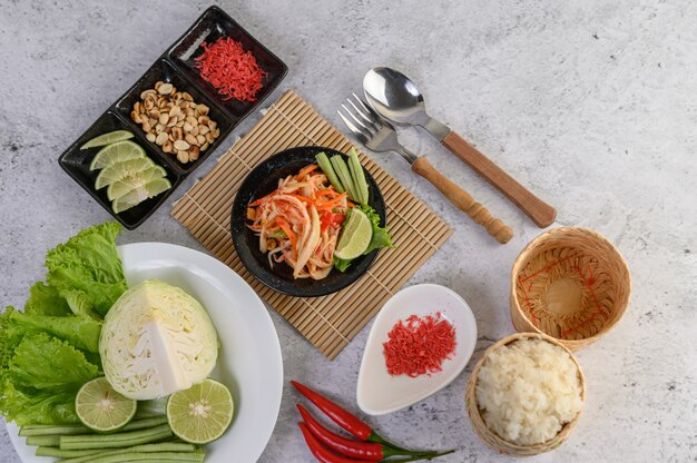 Thai papaya salad in a white plate with sticky rice and dried shrimps