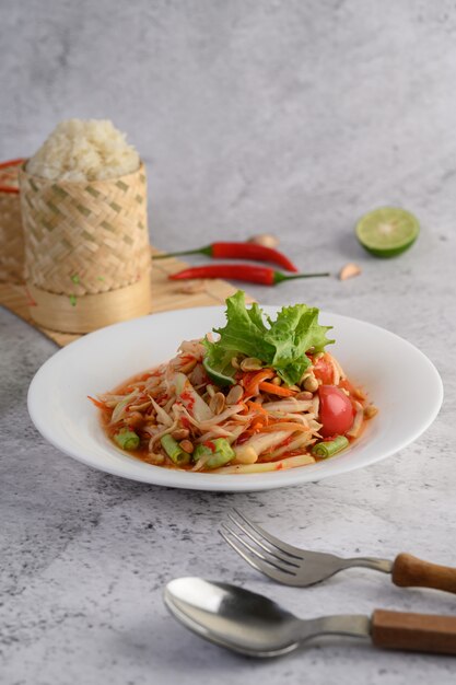 Тайский салат из папайи в белой тарелке с клейким рисом
