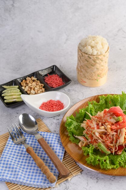 Тайский салат из папайи в деревянной тарелке с клейким рисом