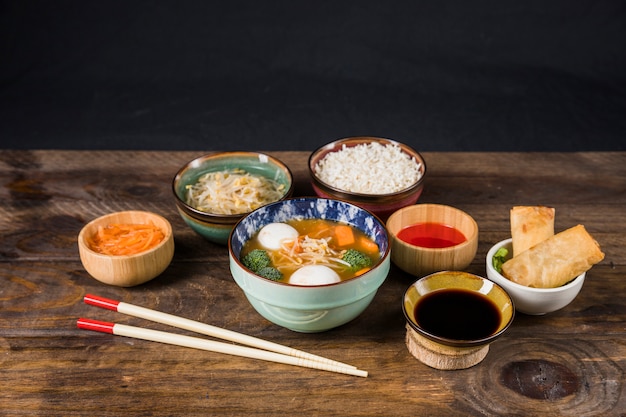 타이 스프; 쌀; 소스; 콩나물; 검은 벽에 테이블에 샐러드와 튀긴 된 춘권