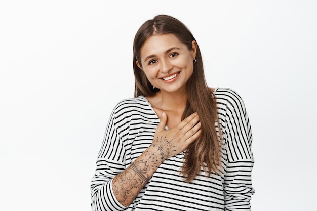 Thank you. Flattered young woman bowing with hand on chest, introduce herself, smiling and receiving praise or compliment, white background