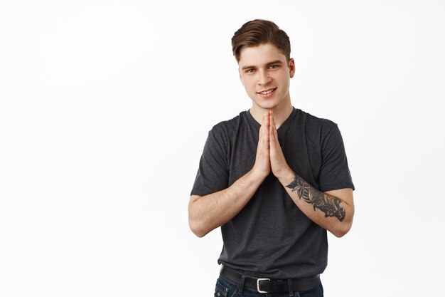 Thank you. Young smiling 20s guy holds hands in pray namaste sign, nod grateful, appreciate help, thanking for something, standing against white background