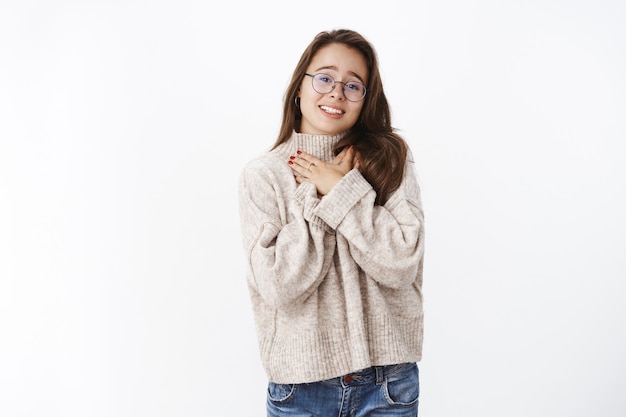 Thankful charming female appreciating tender words holding hands on chest as thanking from heart and soul being touched and grateful feeling happy from heartwarming gestures over gray wall.