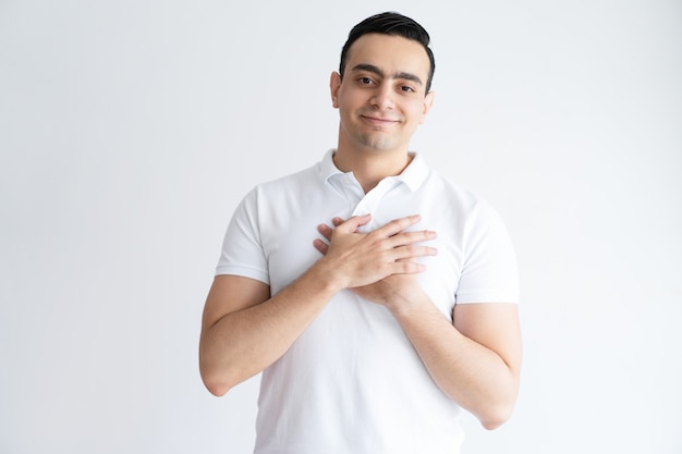 Thankful young man keeping hands on chest and looking at camera.