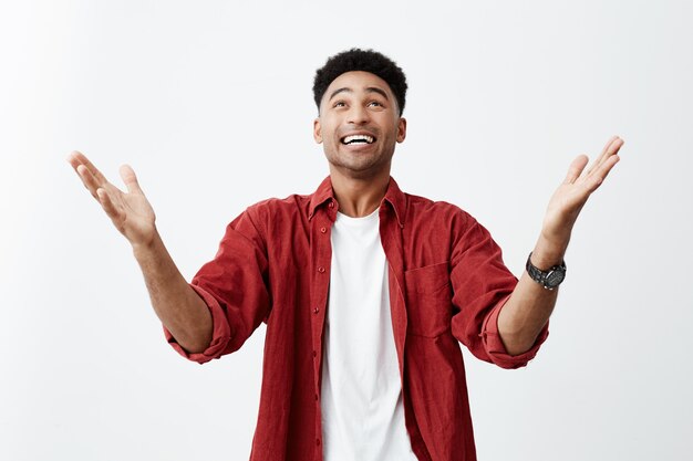 Thanks God. Close up of happy young attractive black-skinned man with afro haircut in casual fashionable outfit spreading hands, being happy that he finally won prize in competition.