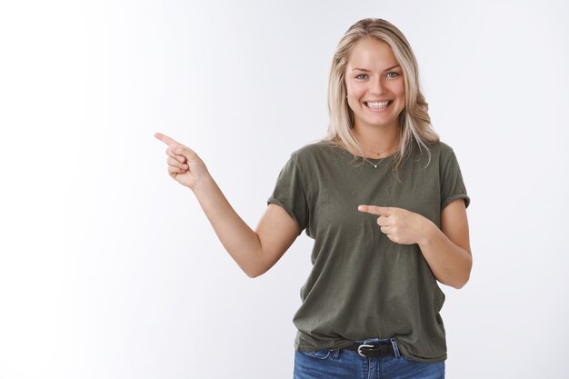 That is way. Portrait of friendly good-looking tanned european adult woman pointing left and smiling as inviting see yourself recommending product indicating advertisement over white background